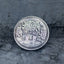 Close-up of the Go To Bed face of a coin engraved with woolly sheep jumping over a moonlit hill, stars and ZZZ symbols, on dark stone surface