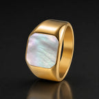 Gold-tone square signet ring with iridescent mother-of-pearl inlay on a black reflective background