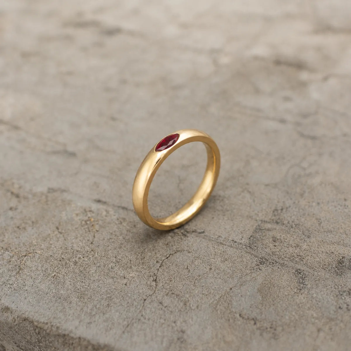 Gold-tone band ring with a red marquise stone shown upright from the side