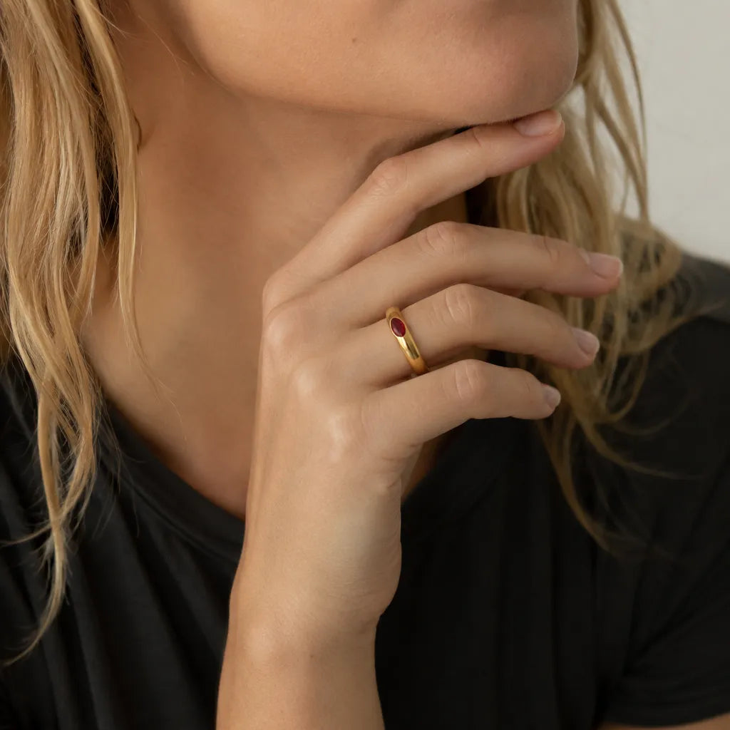 Woman wearing a gold-tone band ring with a red marquise stone in an editorial portrait