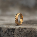 Side view of a gold-tone band ring with a clean reflective faceted texture