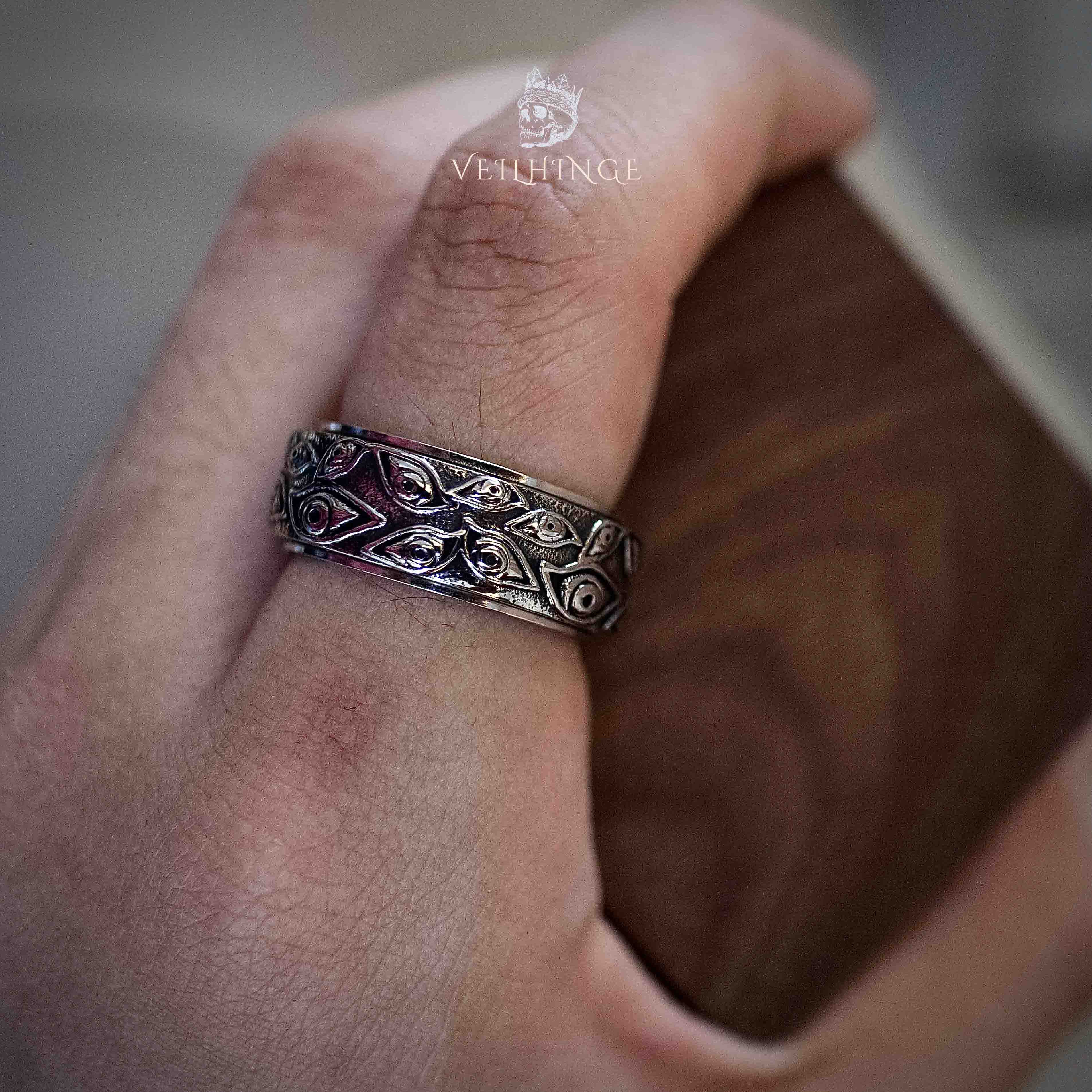 Wide oxidized silver band ring with repeating gothic heart and leaf engravings worn on a finger, photographed in natural light against a wooden surface