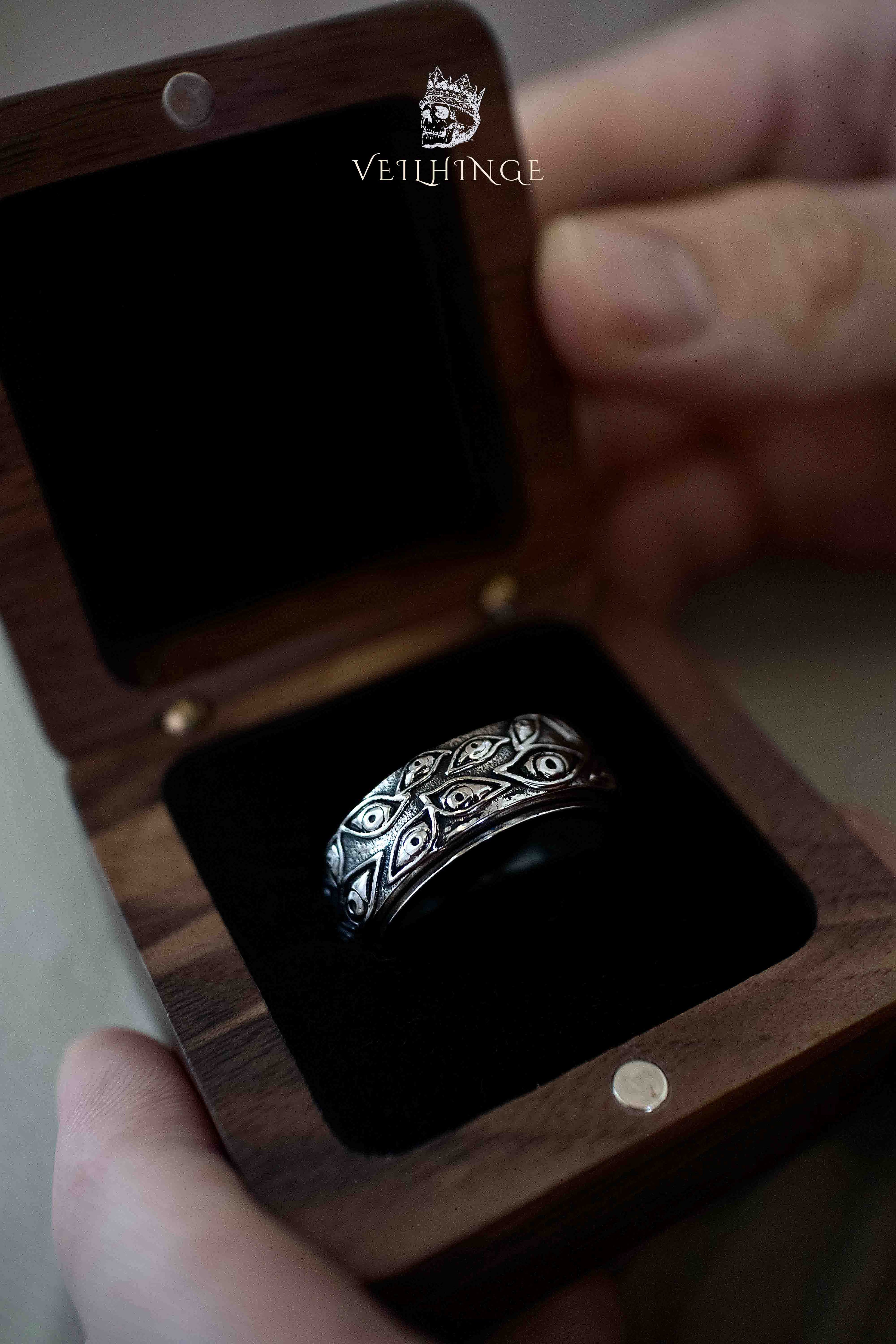 Engraved gothic band ring displayed inside an open wooden jewelry box with black velvet lining, showing the full ring width and pattern