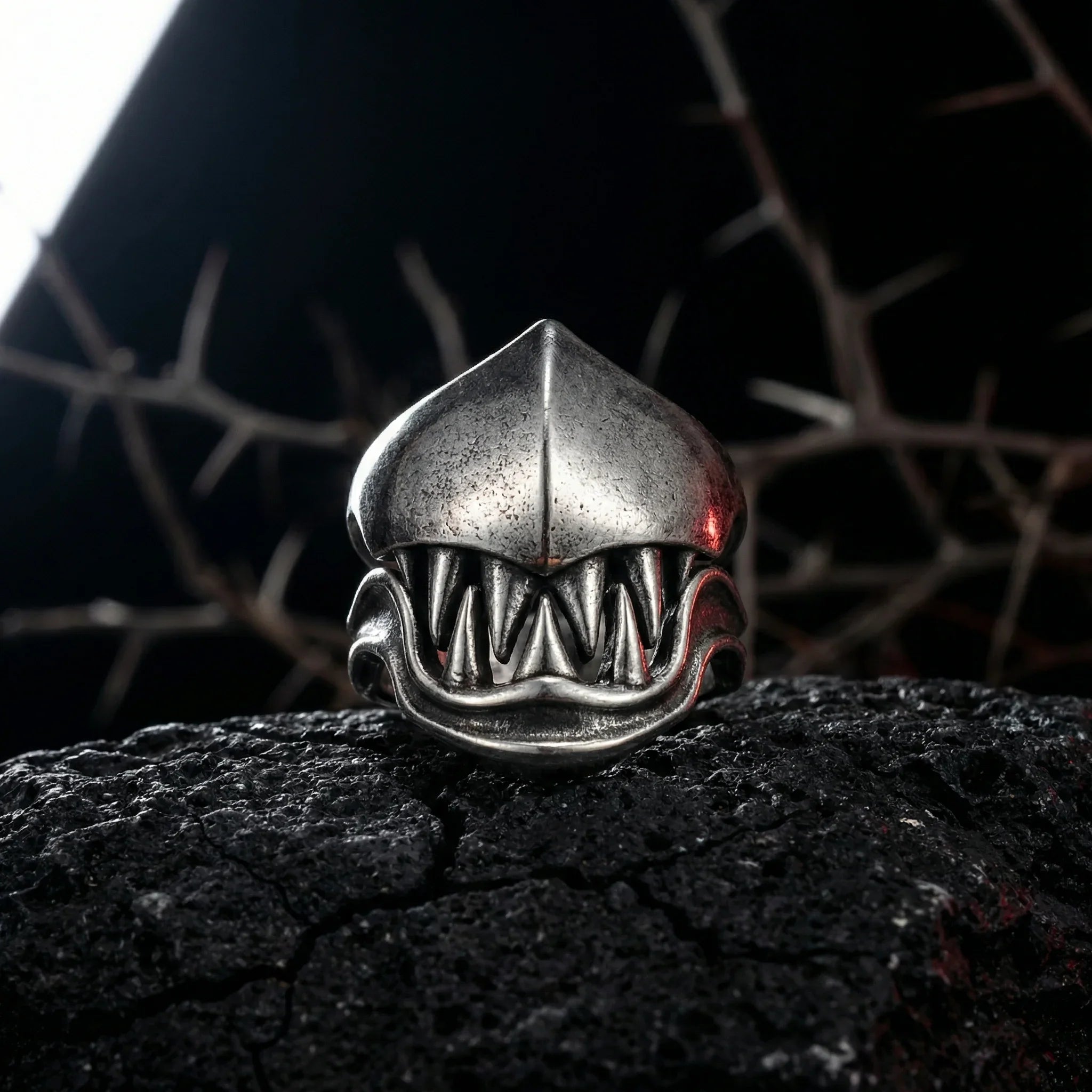 Front view of the gothic monster teeth ring with dramatic fang design placed on cracked dark rock in shadowy gothic setting Imagen principal del producto