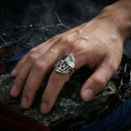 Hand wearing the gothic hinged fang ring resting on dark stone surrounded by chains and feathers, evoking macabre gothic mood