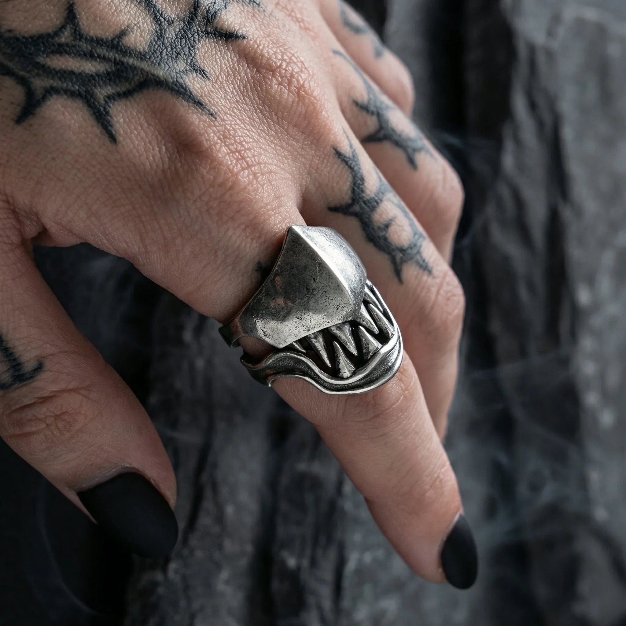 Gothic beast fang ring worn on tattooed hand with black nails, highlighting the hinged monster teeth design in dark gothic atmosphere