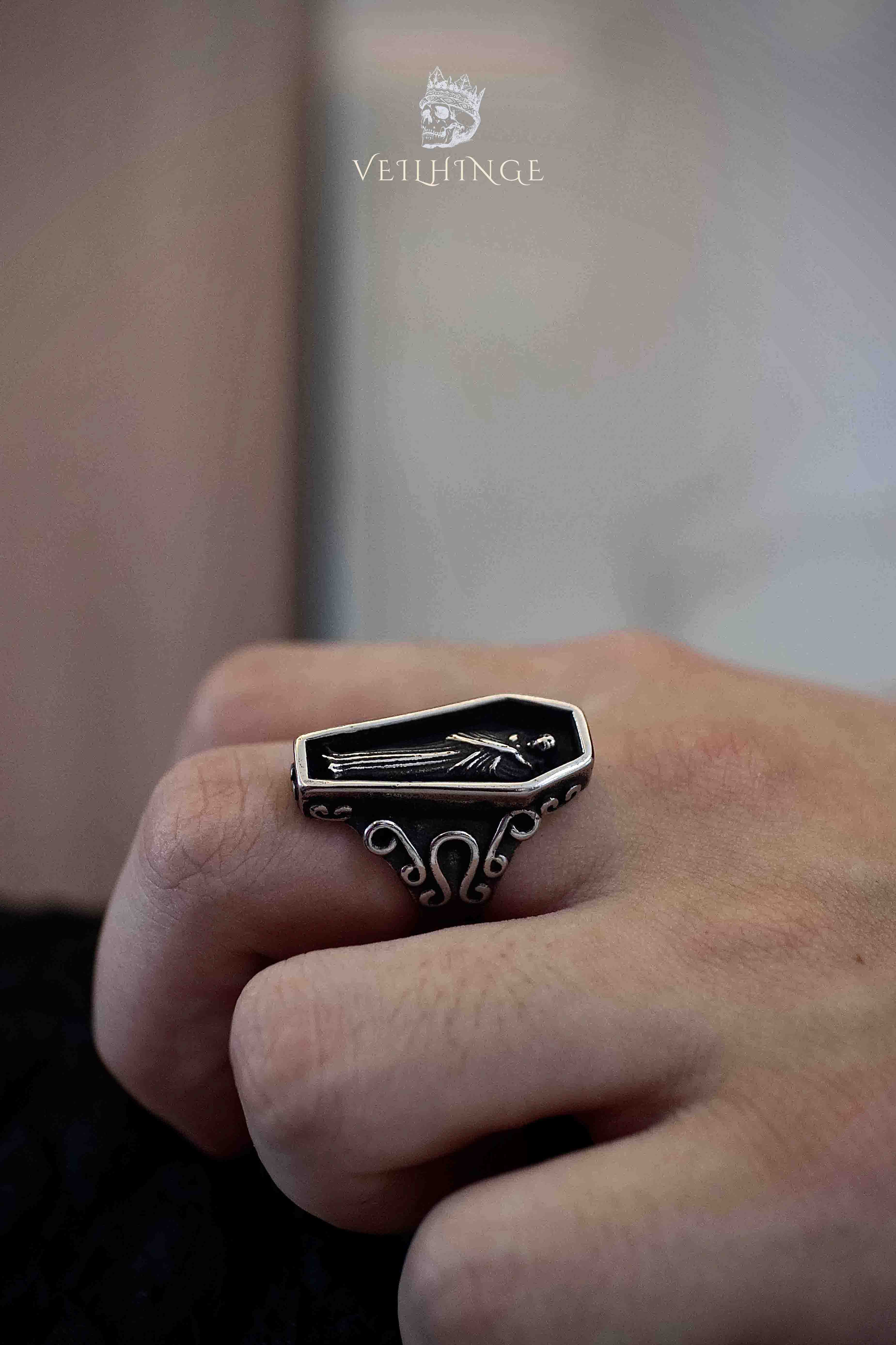 Side view of a gothic coffin ring showing the thick oxidized silver band and ornate scrollwork shoulders, black enamel face with skeletal figure detail
