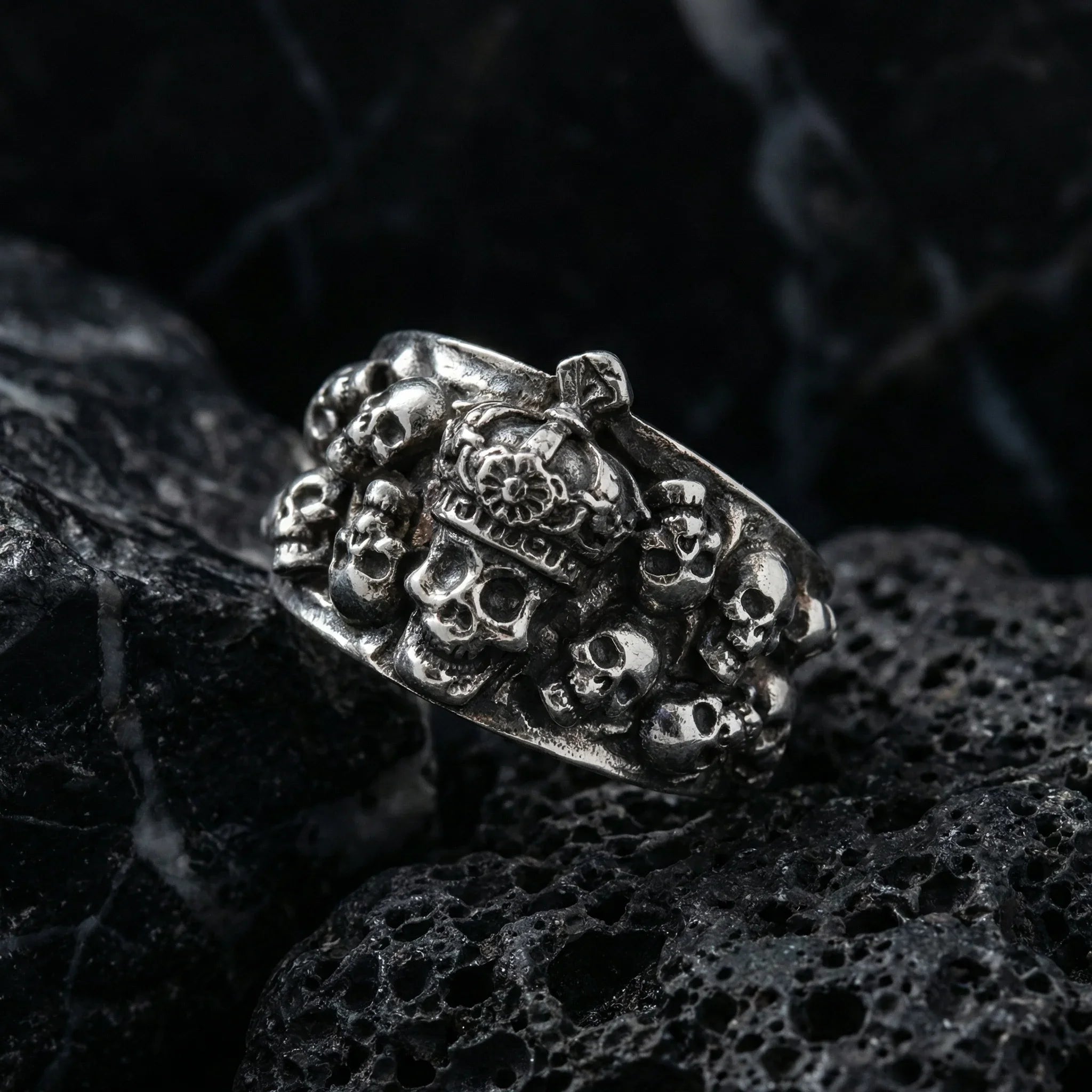 Detailed close-up of the gothic skull crown ring featuring a central crowned skull surrounded by cluster skulls on dark textured rock