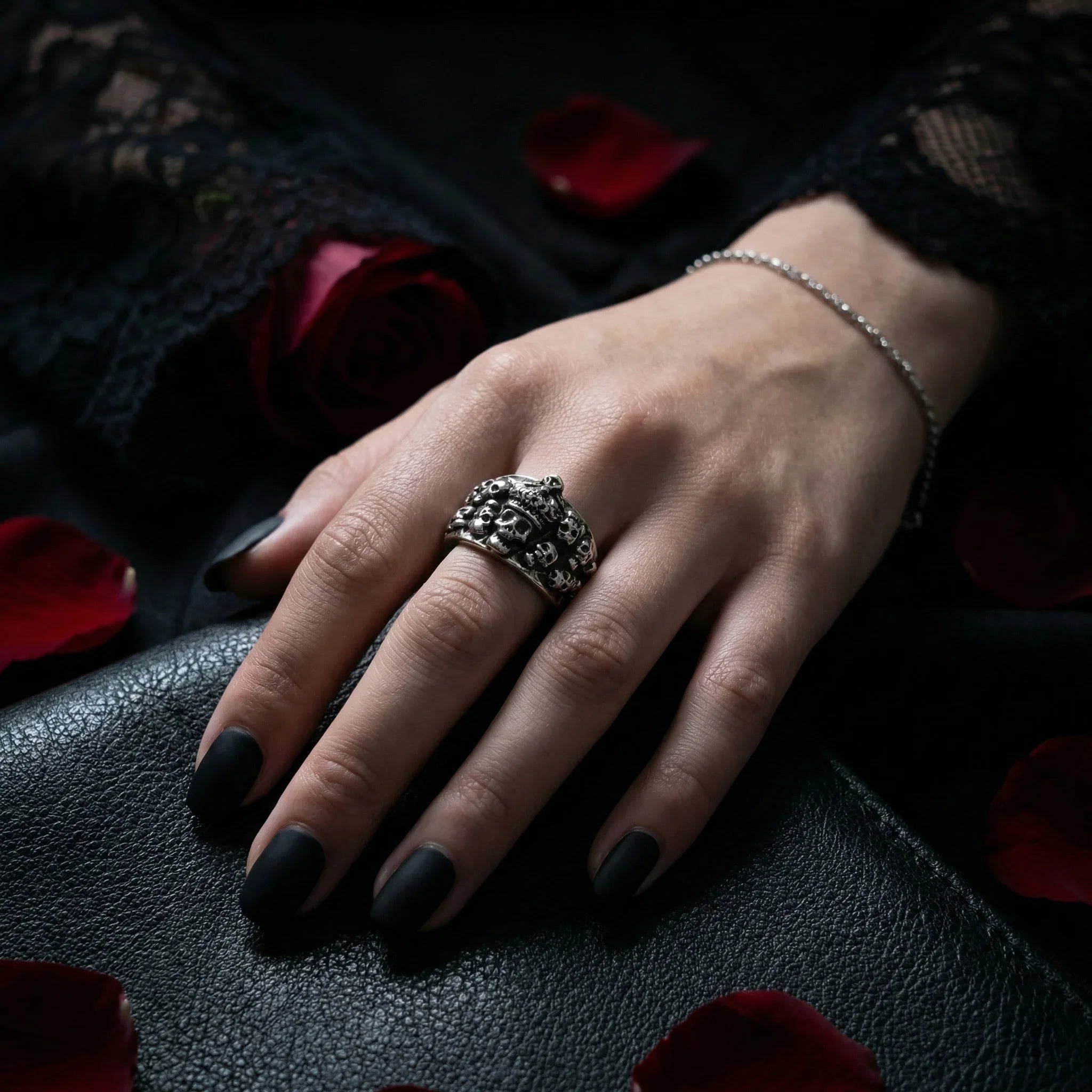 Gothic skull crown ring worn on hand with black nails, styled with black lace and red rose petals in dark moody atmosphere