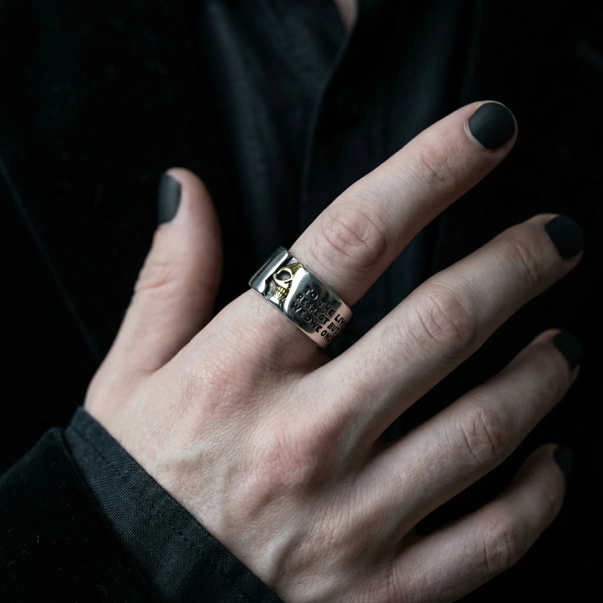 Hand in black velvet sleeve wearing the Gothic Voltaire skull ring with gold skull detail and engraved text
