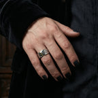 Hand in black velvet sleeve wearing the Gothic Voltaire skull ring with gold skull detail and engraved text