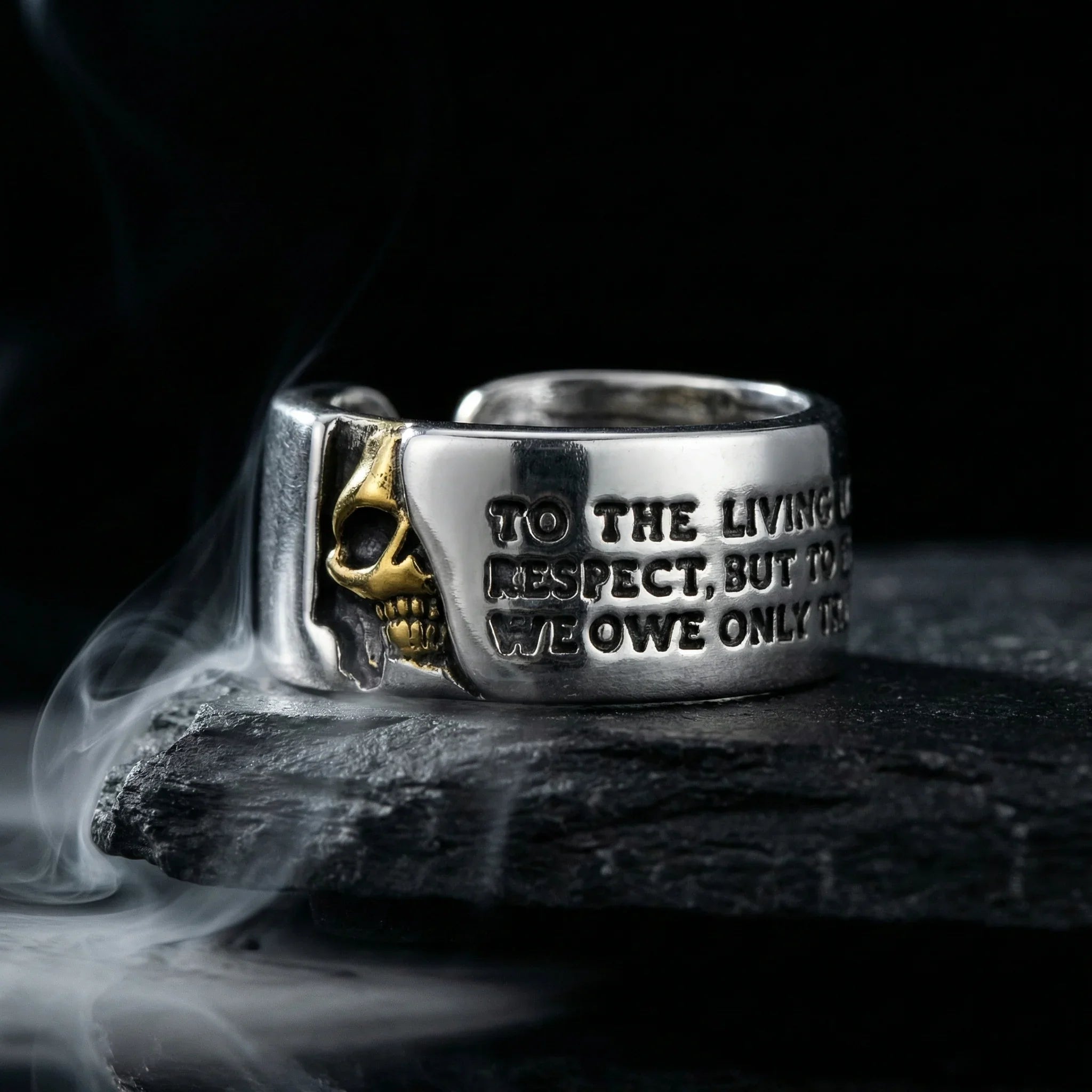 Gothic Voltaire skull ring with gold skull and engraved quote on dark rock with smoke