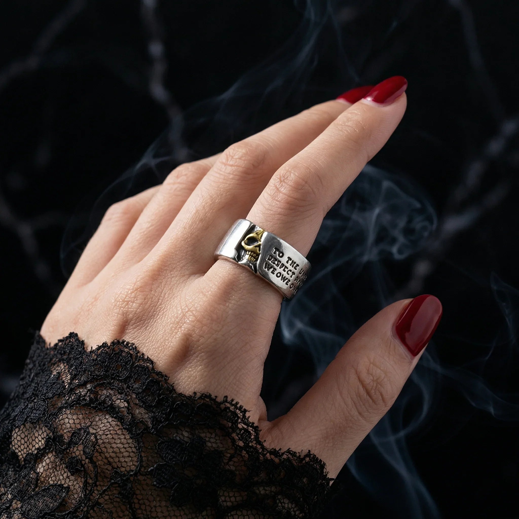 Hand with red nails and black lace wearing the Gothic Voltaire skull ring in smoky dark atmosphere
