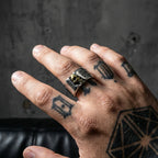 Tattooed hand wearing the Gothic Voltaire skull ring with engraved quote "To the living we owe respect, but to the dead we owe only the truth"
