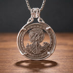 grim reaper hobo coin pendant necklace — robed reaper figure with scythe hand-cut on 1921 Morgan Dollar coin face, E pluribus unum inscription, crescent moon and sun detail, four-prong open frame, skull bail, antique silver tone, dark wood surface