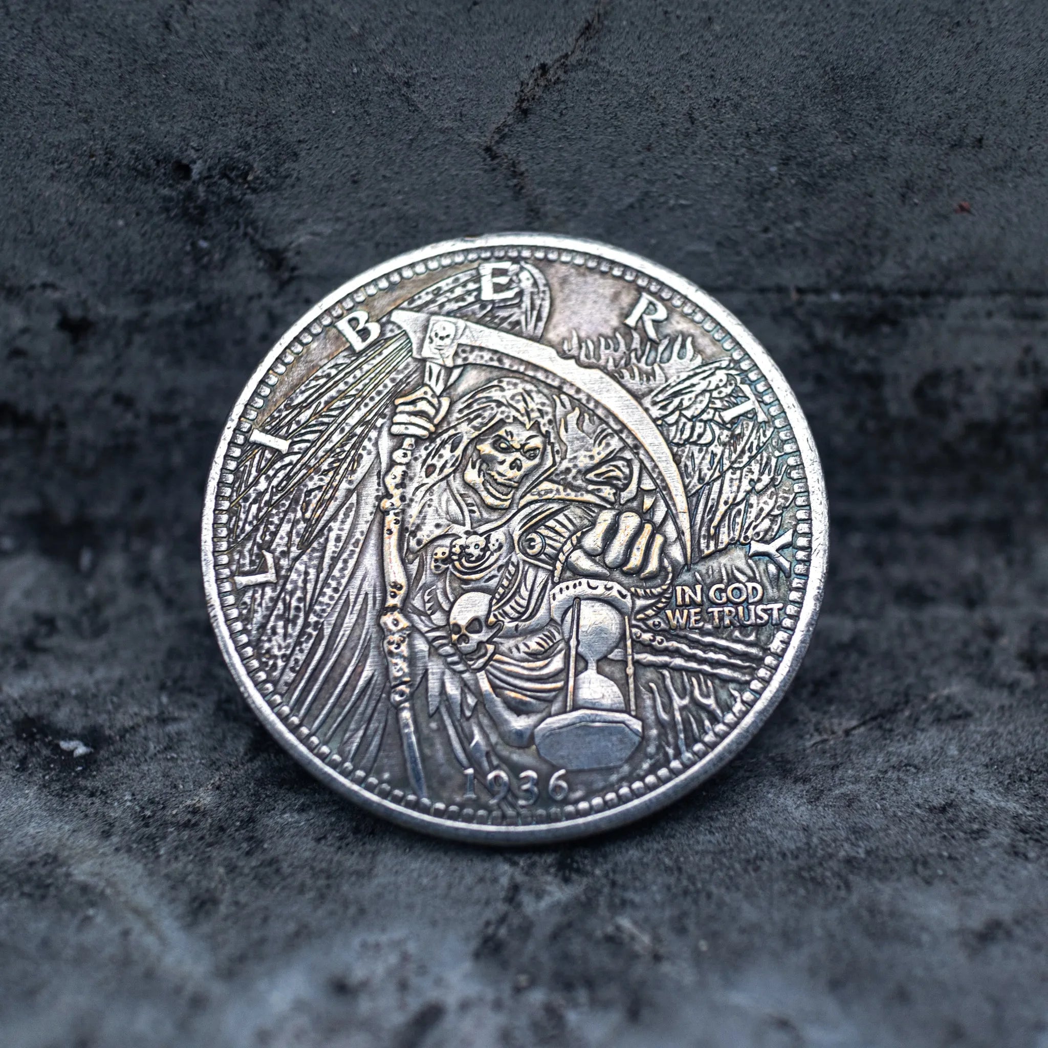 Close-up of a coin engraved with a winged skeletal Grim Reaper raising a scythe, holding an hourglass, skull at feet, In God We Trust, Liberty border, dated 1936