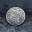 Close-up of a coin engraved with a winged skeletal Grim Reaper raising a scythe, holding an hourglass, skull at feet, In God We Trust, Liberty border, dated 1936