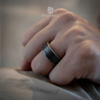 Close-up of a hammered oxidized band ring on a clenched fist, showing the ring's dark matte surface texture and thick rounded edges