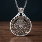 biker skull coin pendant necklace — shield badge with skull and wings hand-cut on coin face, E pluribus unum 1893 inscription, four-prong open frame, skull bail, antique silver tone, dark wood surface