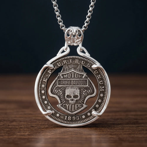 biker skull coin pendant necklace — shield badge with skull and wings hand-cut on coin face, E pluribus unum 1893 inscription, four-prong open frame, skull bail, antique silver tone, dark wood surface