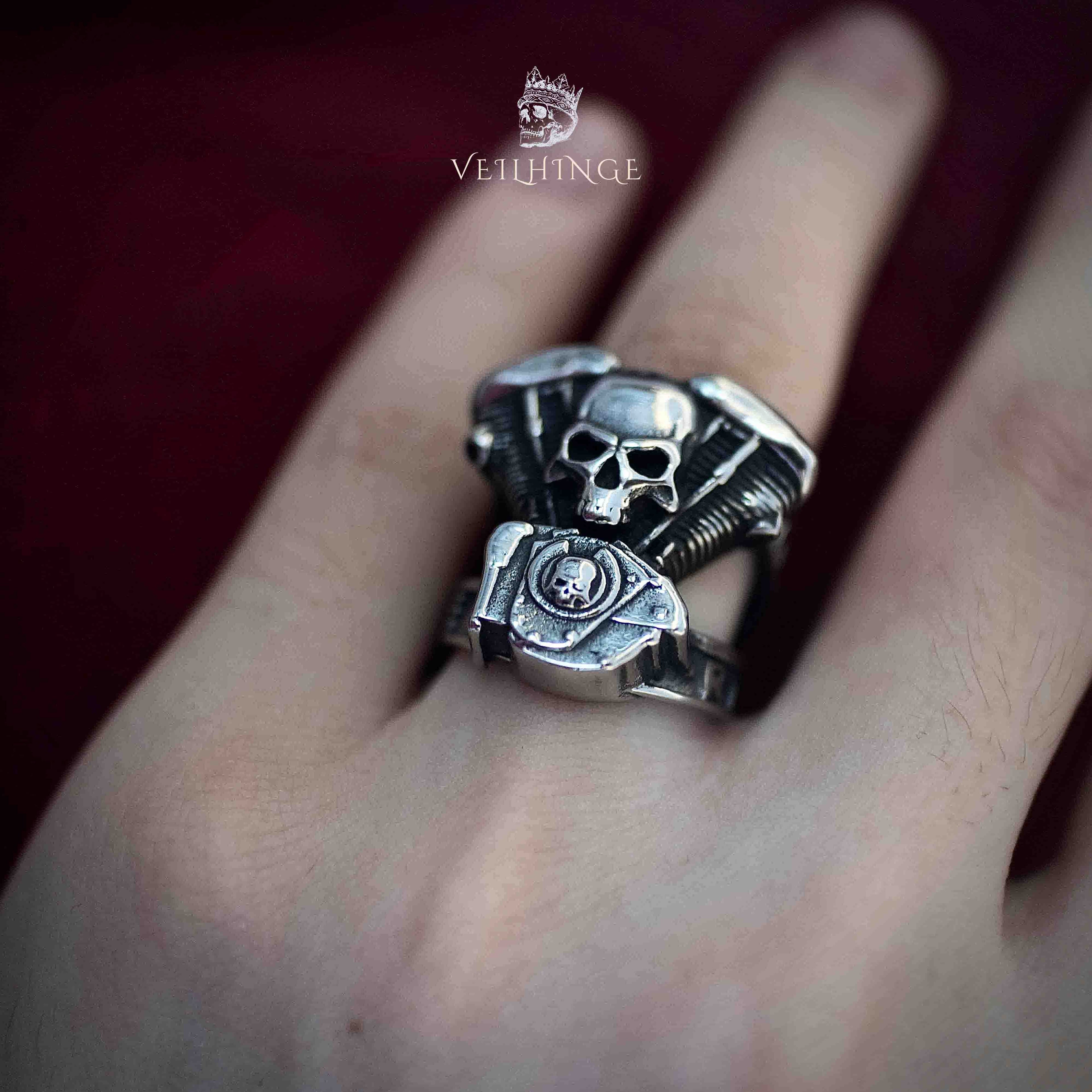 Live to Ride skull ring worn on an outstretched finger against a deep red background, engine and skull motif clearly visible