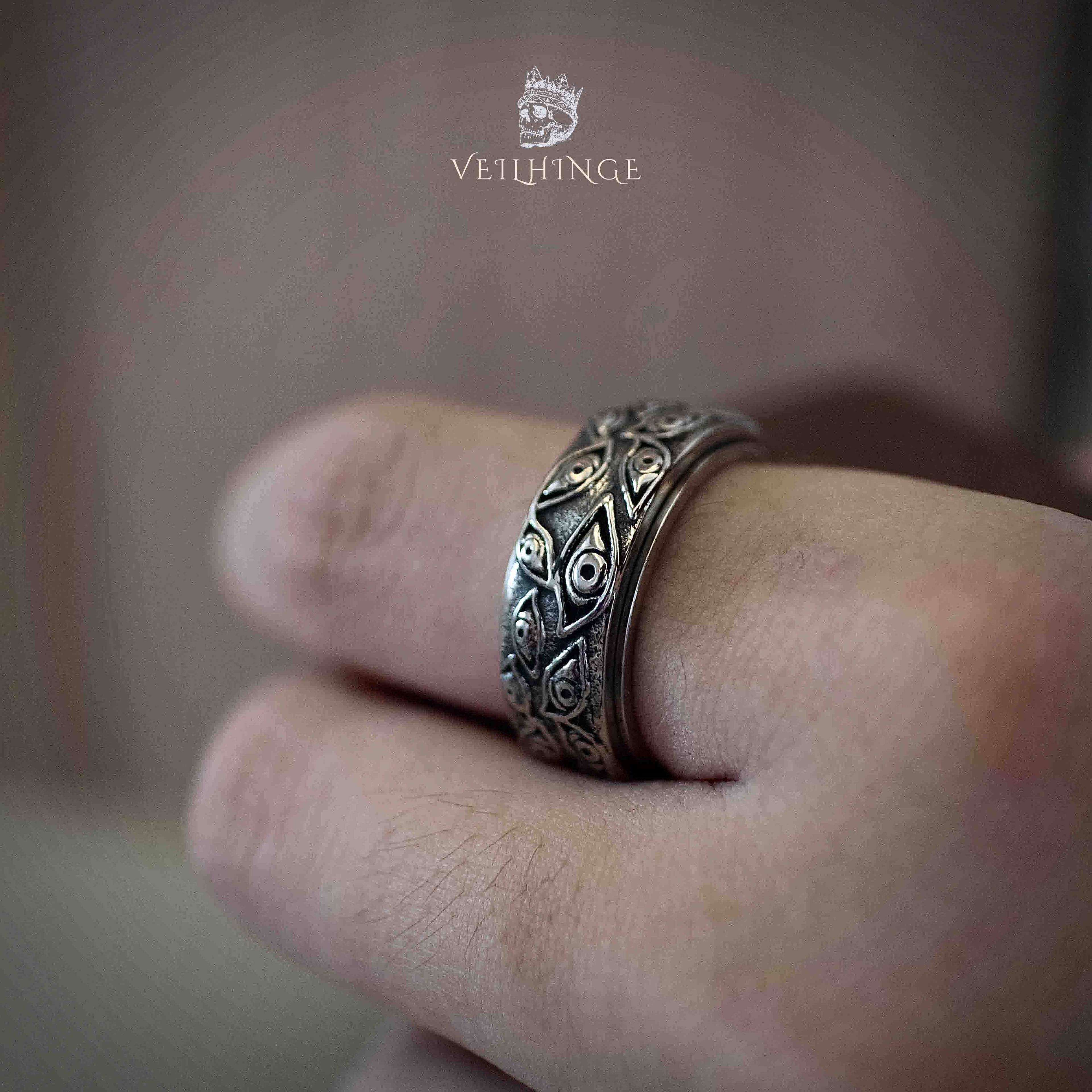 Front view of a wide silver band ring fully engraved with medieval-style heart and eye motifs, oxidized dark fill highlighting the pattern detail