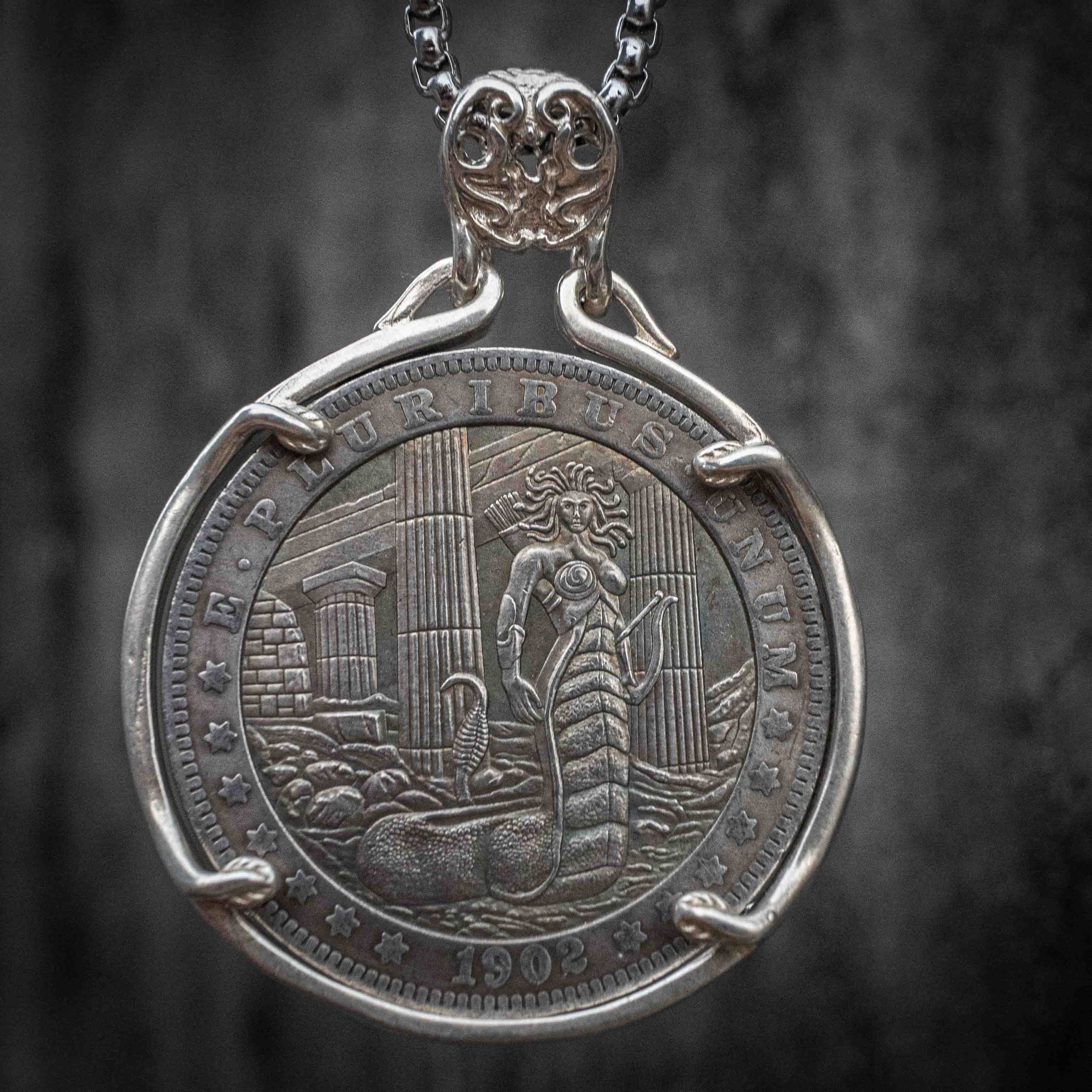 Coin pendant engraved with full-body Medusa with serpent tail coiled among ancient temple columns, dated 1902, set in a four-prong bezel on a chain Main image