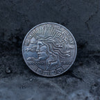 Close-up of a coin engraved with Medusa in profile, serpent hair coiling outward, Liberty above, In God We Trust below, dated 1923, on dark stone