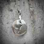 Back of Medusa pendant showing smooth oval silver surface with subtle raised relief — clean reverse finish, box chain clasp visible