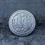 Close-up of a coin engraved with Medusa standing with coiled serpent tail among crumbling stone columns, E Pluribus Unum border, dated 1902