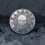 Memento Mori coin with ornate skull engraving and baroque border detail, displayed on dark textured stone