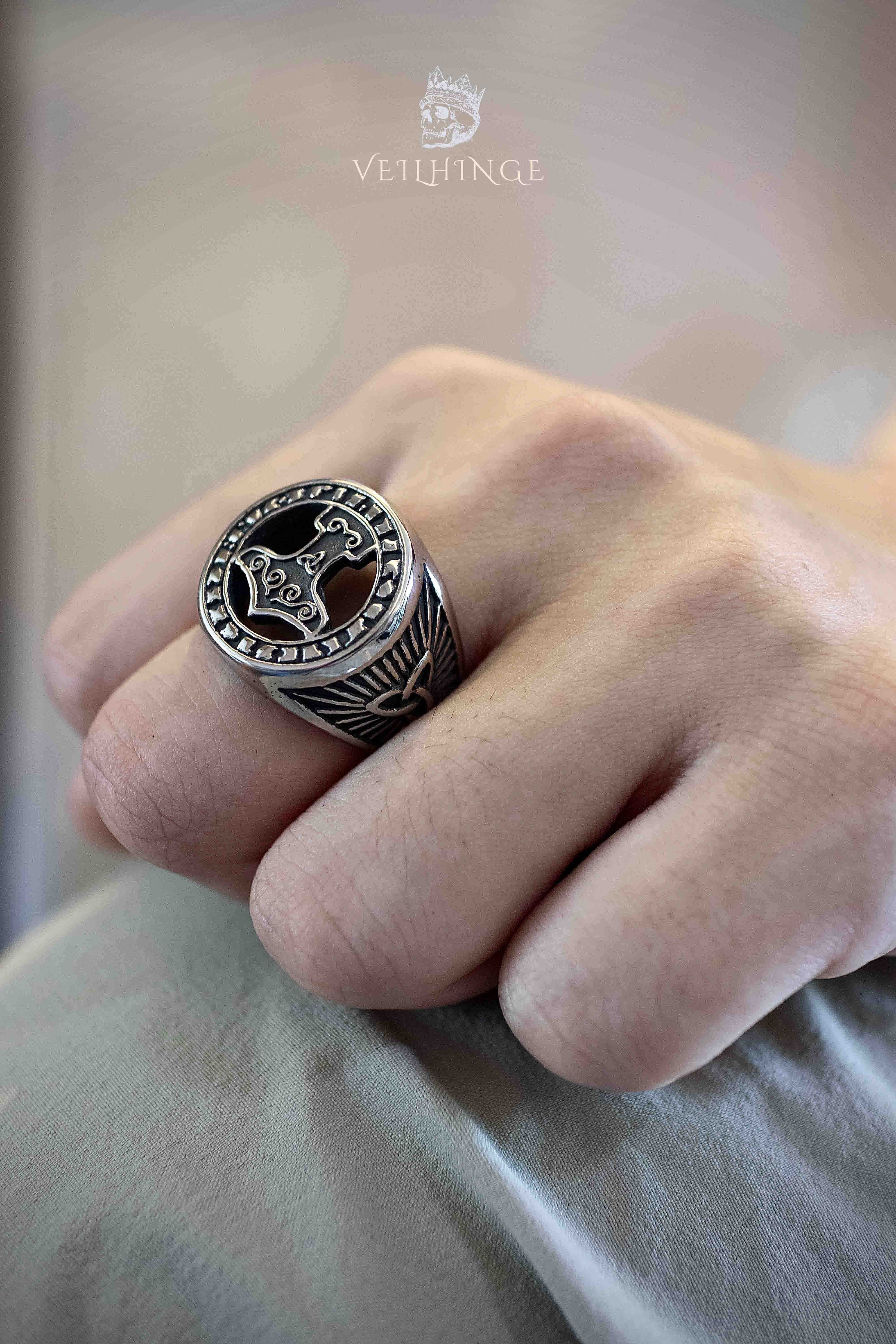 Thor's hammer Mjolnir signet ring with black enamel face and raven wing engravings on the shoulders, large round face with runic border worn on a middle finger resting on fabric
