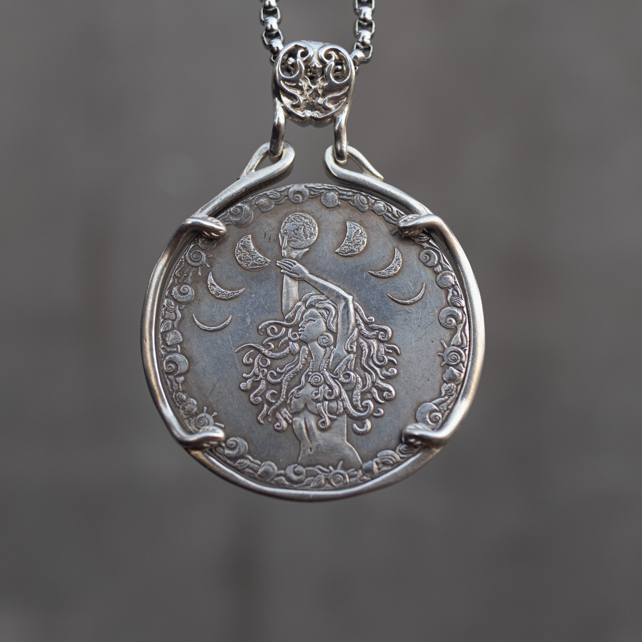 Coin pendant engraved with a moon goddess figure holding a full moon, surrounded by crescent moon phases and cloud border, set in a four-prong bezel on a decorative chain Main image