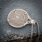 Heraldic serpent coin pendant laid flat on dark stone showing the Morgan Dollar eagle reverse with United States of America and One Dollar inscription