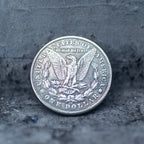 A silver-colored United States one dollar coin featuring an eagle and laurel wreath, photographed standing upright on a dark textured surface.