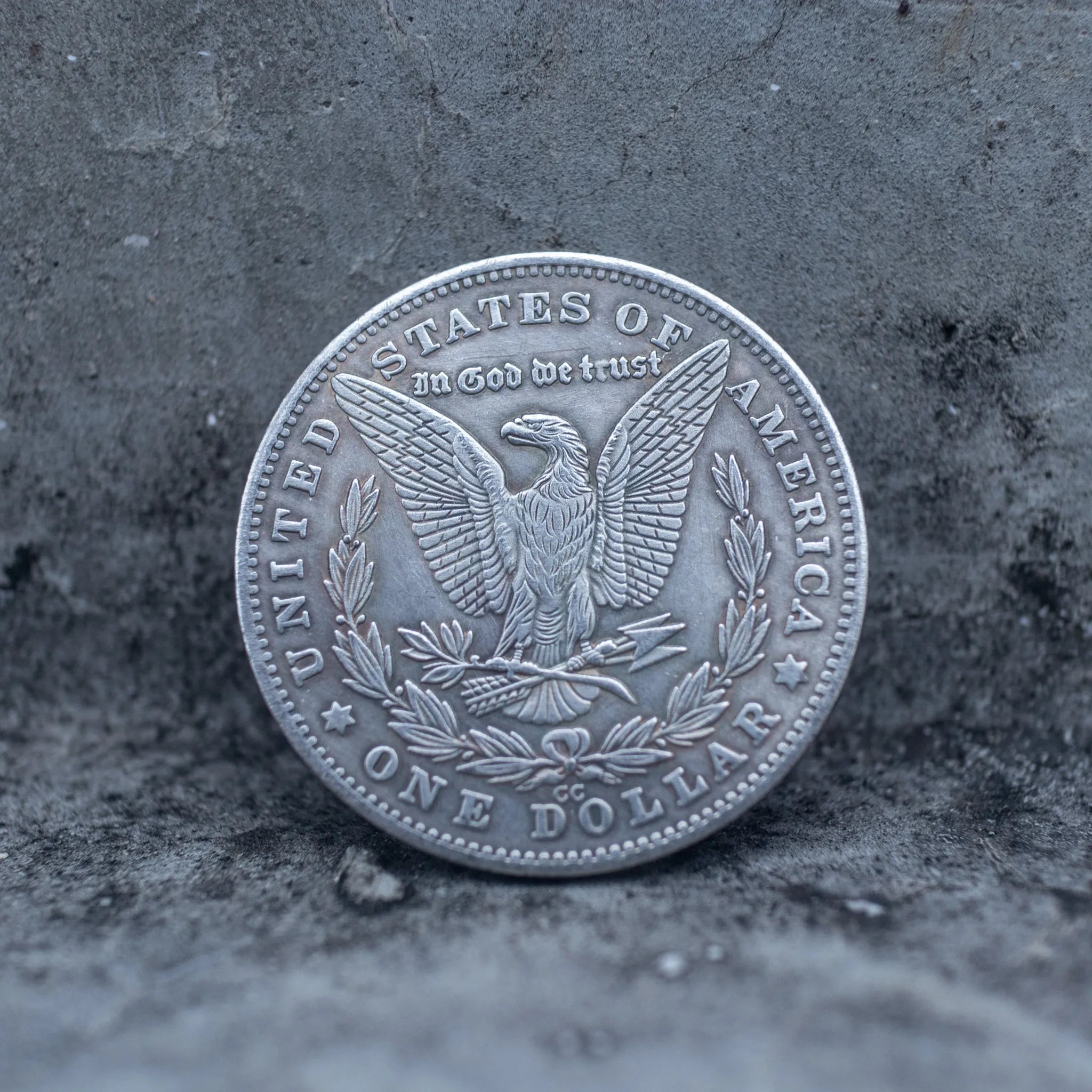 Morgan Dollar reverse showing the American eagle with spread wings, In God We Trust, United States of America, and One Dollar denomination on dark stone