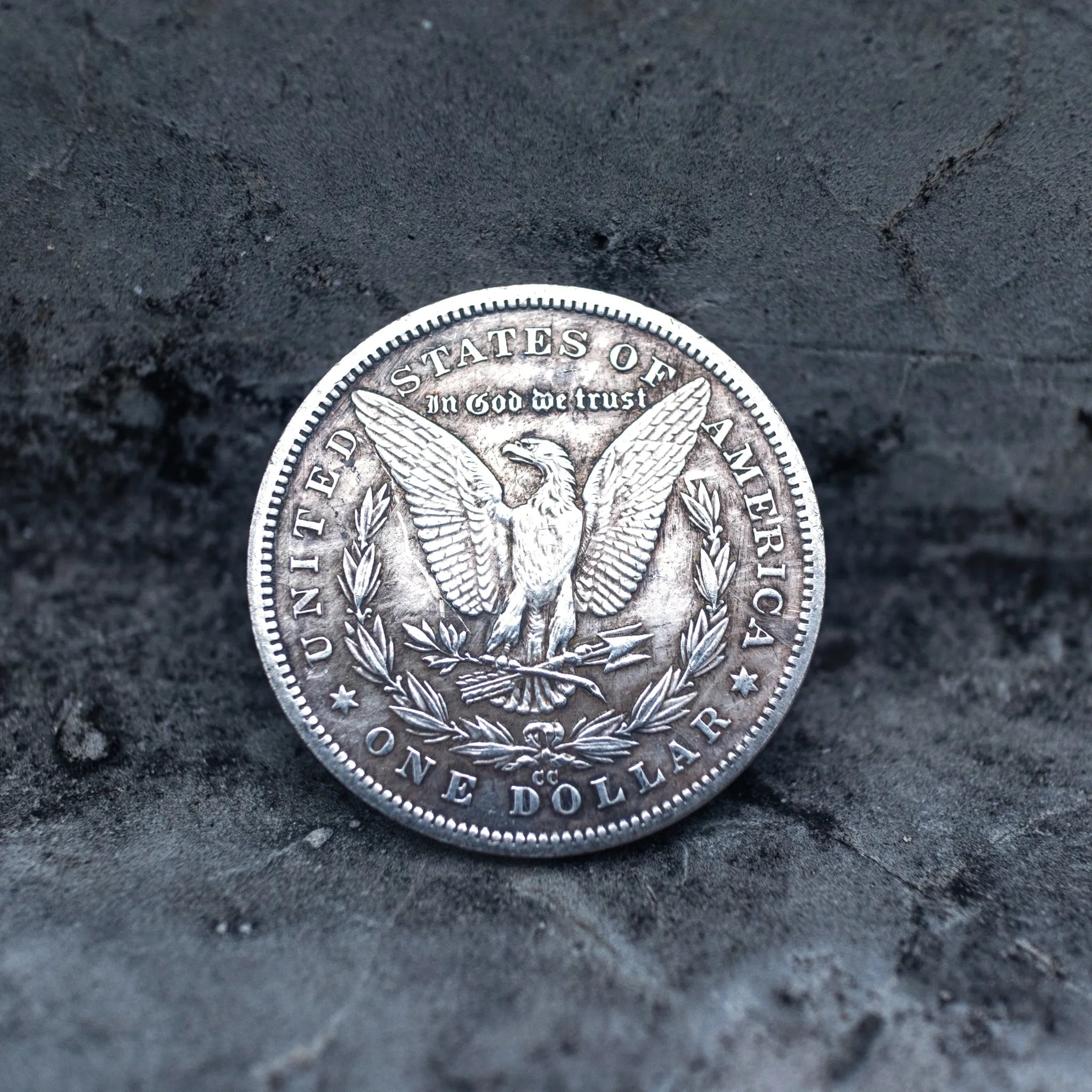 Morgan Dollar reverse showing the American eagle with spread wings, In God We Trust, United States of America, and One Dollar denomination on dark stone surface