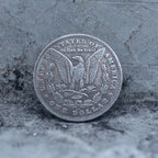 Morgan Dollar reverse showing the American eagle with spread wings, In God We Trust, United States of America, and One Dollar denomination on dark stone