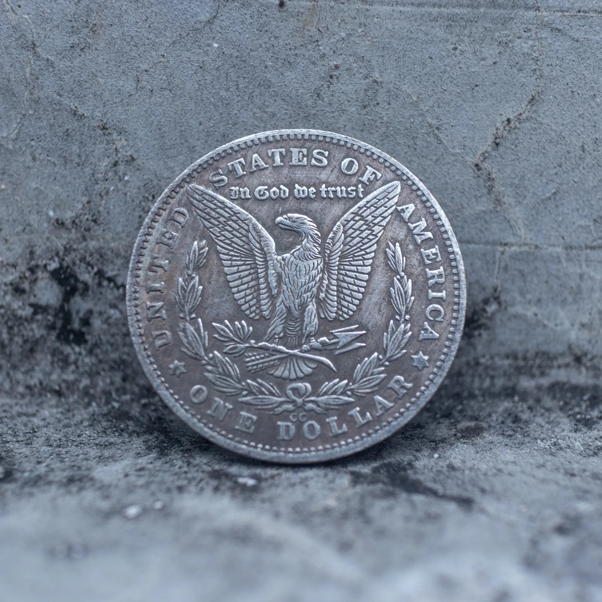 Morgan Dollar reverse showing the American eagle with spread wings, In God We Trust, United States of America, and One Dollar denomination on dark stone