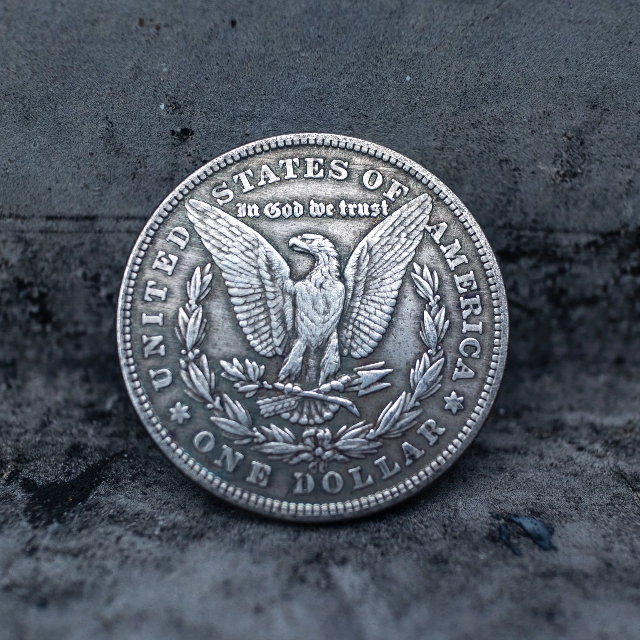 Morgan Dollar reverse showing the American eagle with spread wings, In God We Trust, United States of America, and One Dollar denomination on dark stone