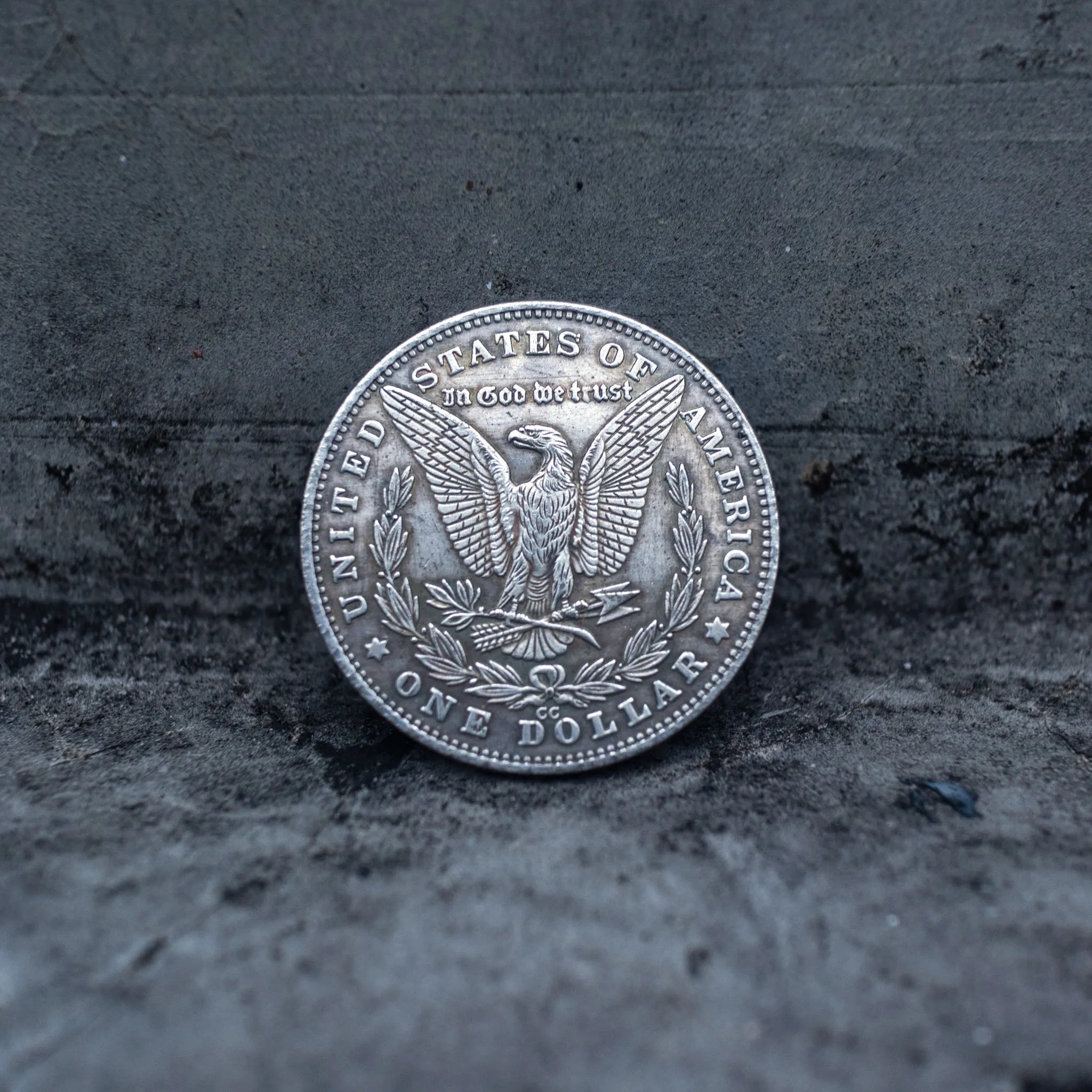 Morgan Dollar reverse showing the American eagle with spread wings, In God We Trust, United States of America, and One Dollar denomination on dark stone