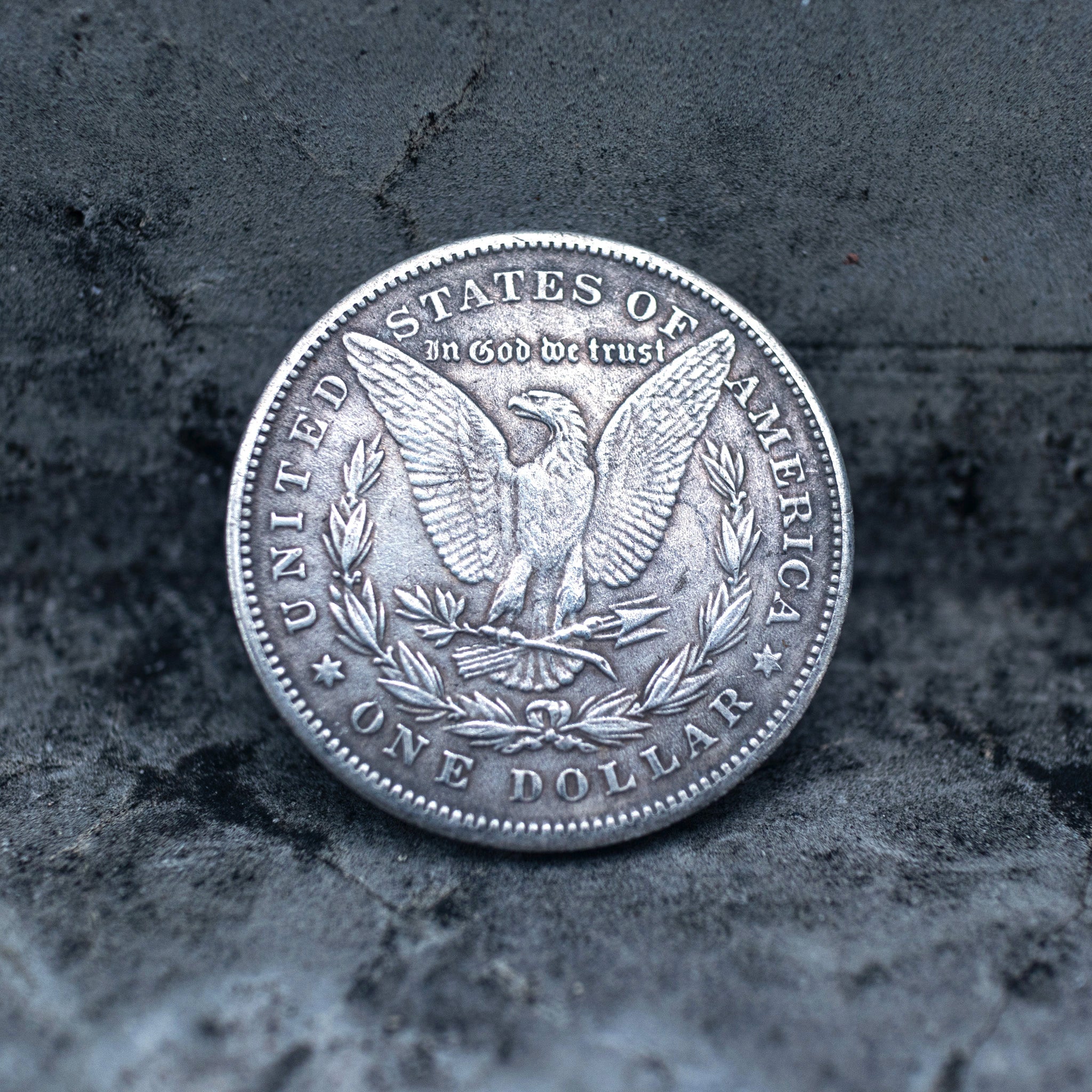 Morgan Dollar reverse showing the American eagle with spread wings, In God We Trust, United States of America, and One Dollar denomination on dark stone
