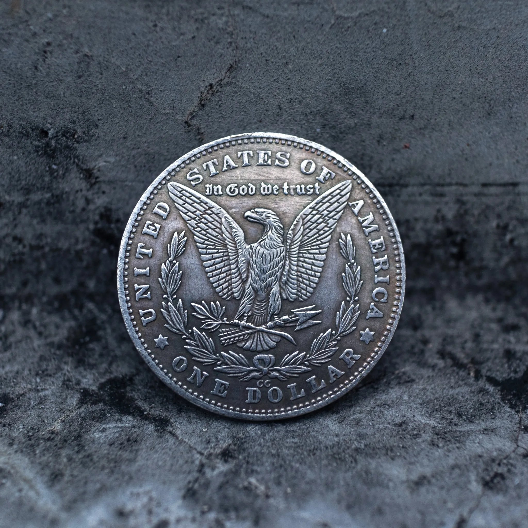 Morgan Dollar reverse showing the American eagle, In God We Trust, United States of America, and One Dollar denomination on dark stone surface