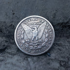Morgan Dollar reverse showing the American eagle with spread wings, In God We Trust, United States of America, and One Dollar denomination on dark stone
