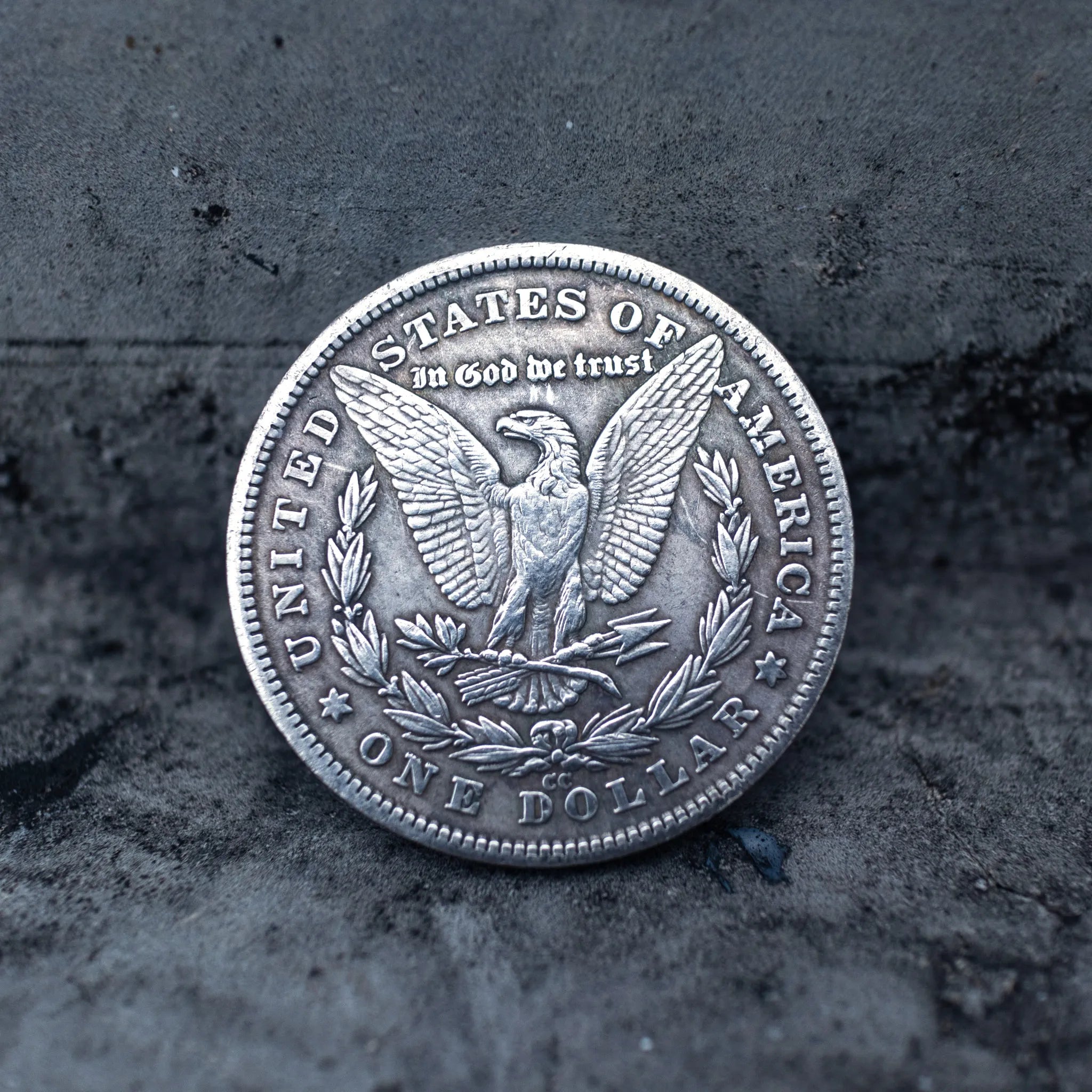 Morgan Dollar reverse showing the American eagle with spread wings, In God We Trust, United States of America, and One Dollar denomination on dark stone