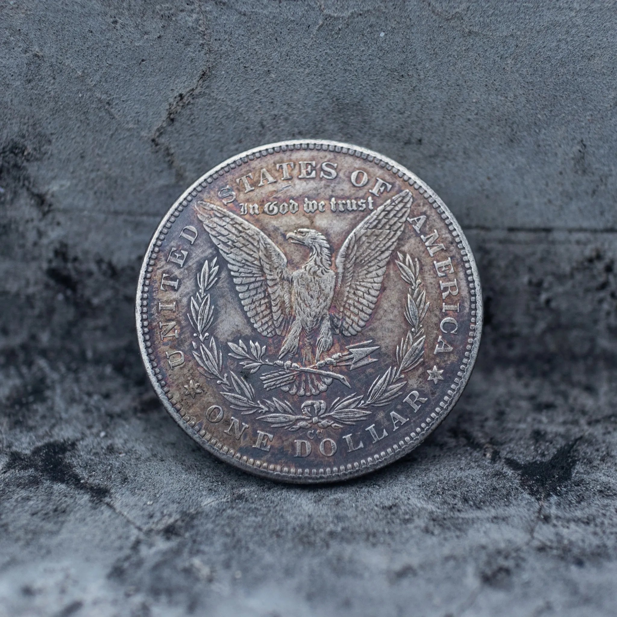 Morgan Dollar reverse showing the American eagle with spread wings, In God We Trust, United States of America, and One Dollar denomination on dark stone