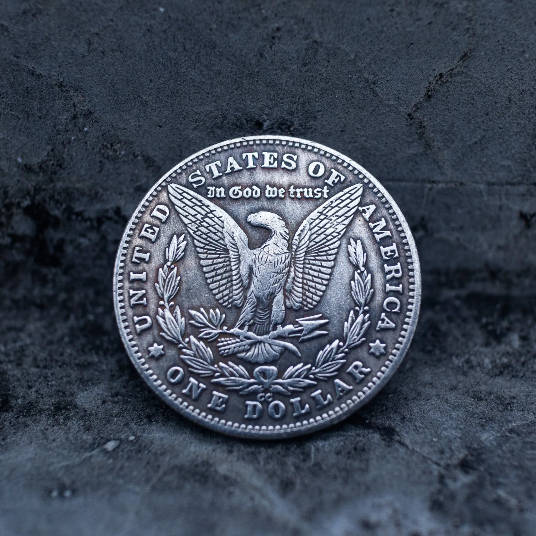 Morgan Dollar reverse with American eagle, In God We Trust and United States of America inscriptions, One Dollar denomination on dark stone surface