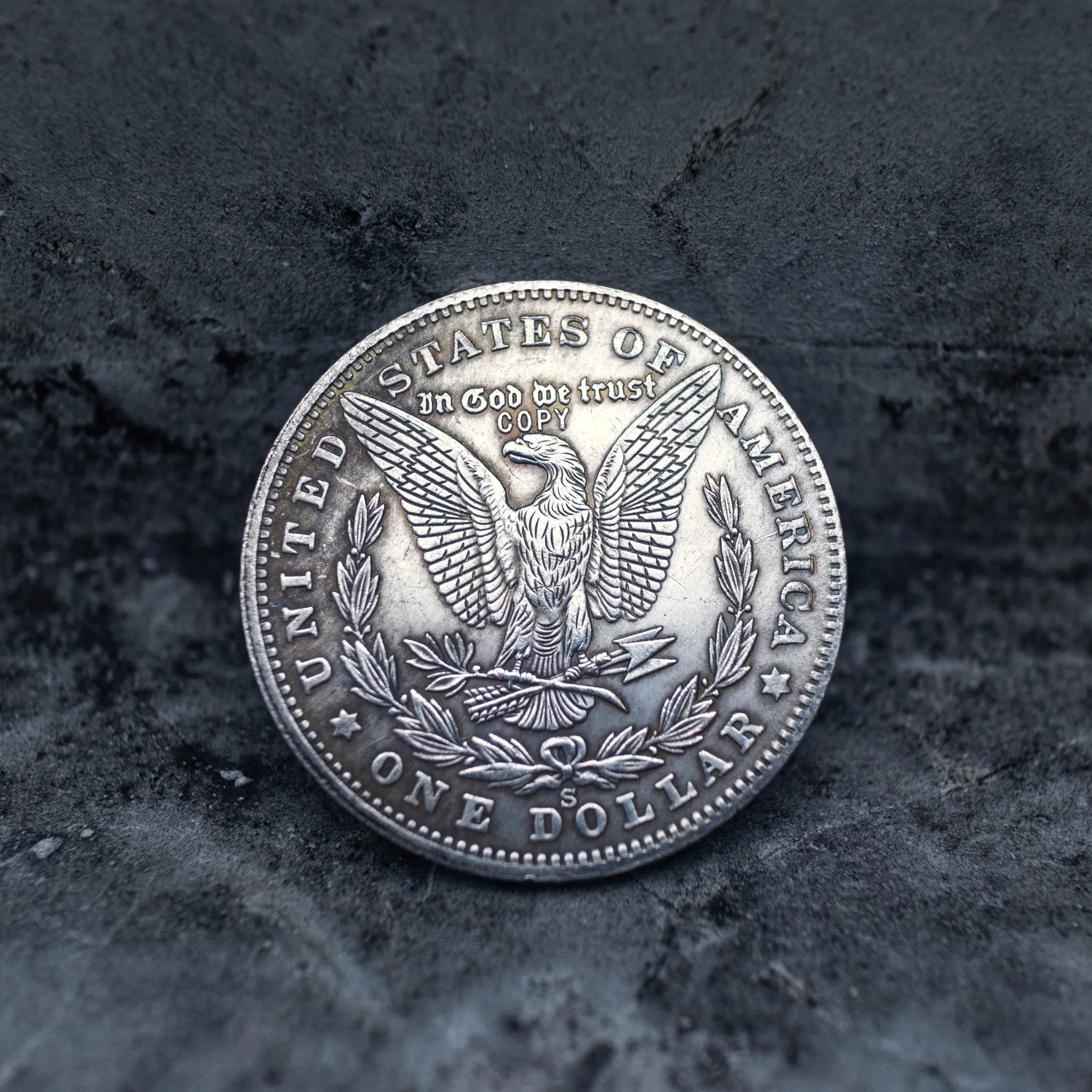 Morgan Dollar reverse with American eagle, In God We Trust and United States of America inscriptions, One Dollar denomination on dark stone