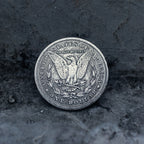 A silver-colored United States one dollar coin with the eagle design, photographed upright on a dark textured stone surface.