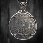 A silver pendant necklace featuring a coin-style medallion with an eagle and the text 'United States of America' and 'One Dollar,' suspended from a dark chain against a dark textured background.